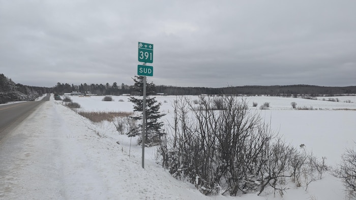 Dans un décor enneigé, on peut apercevoir un terrain vague, un panneau de la route 391 et une partie de la route.