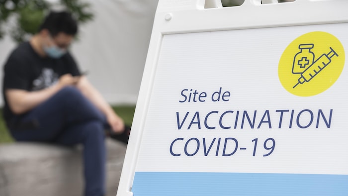 Un homme regarde son téléphone. Une pancarte indique la présence d'un centre de vaccination contre la COVID-19.