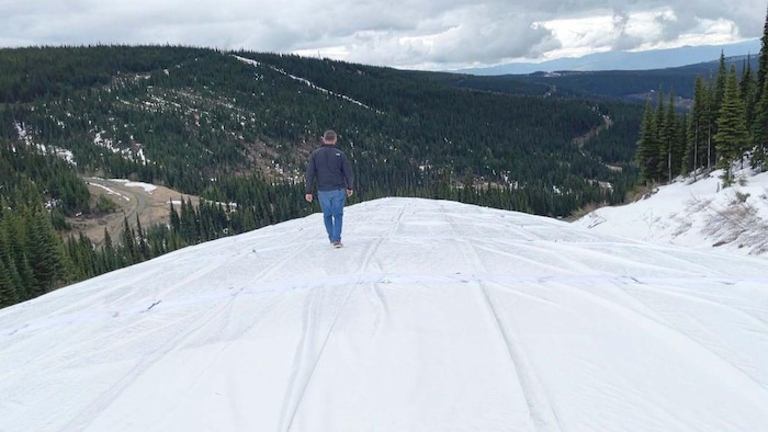 Un homme marche sur une pile de neige enveloppée par une couverture isolante.