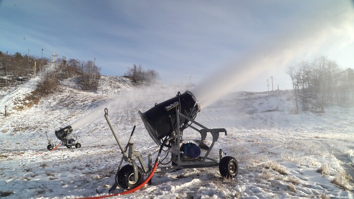 Un canon à neige qui déverse de la neige sur la piste du ski.