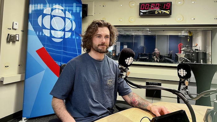 Un homme est assis devant un micro dans un studio de radio.