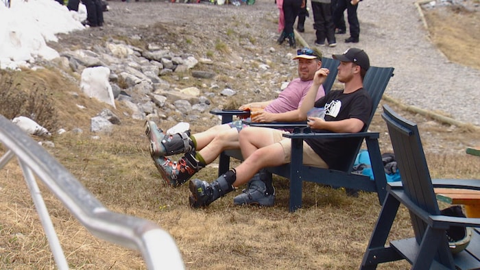 Deux hommes assis dans des chaises. Ils sont en shorts et portent des bottes de ski. 