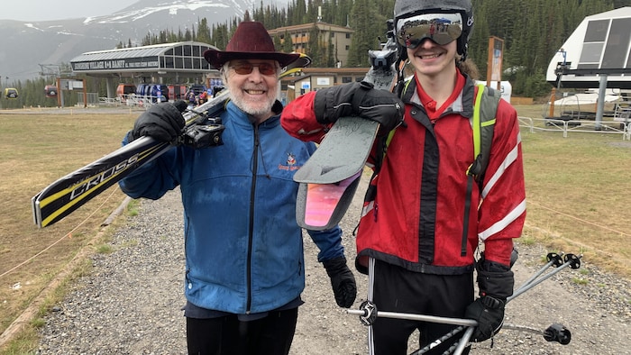 Un grand-père et son petit-fils avec leur équipement de ski sur l'épaule. 