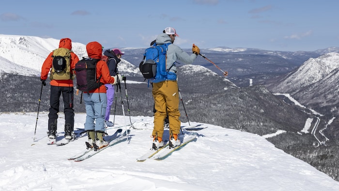 Un groupe de skieurs au sommet d'un mont observent la vue enneigée du parc national de la Gaspésie.