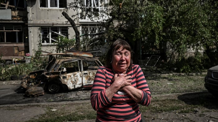 Une femme tient un document sur son corps devant un immeuble détruit.