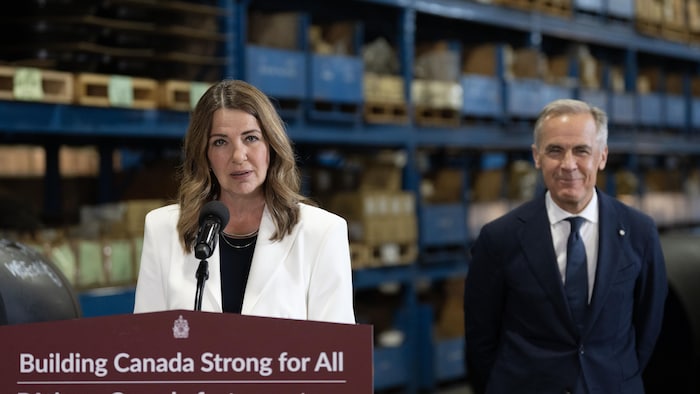 La première ministre de l’Alberta, Danielle Smith, se tient devant un pupitre tandis que, à sa gauche, se tient debout le premier ministre du Canada, Mark Carney, lors de l’annonce des détails concernant un nouveau pipeline, à Calgary, le 2 juillet 2026.
