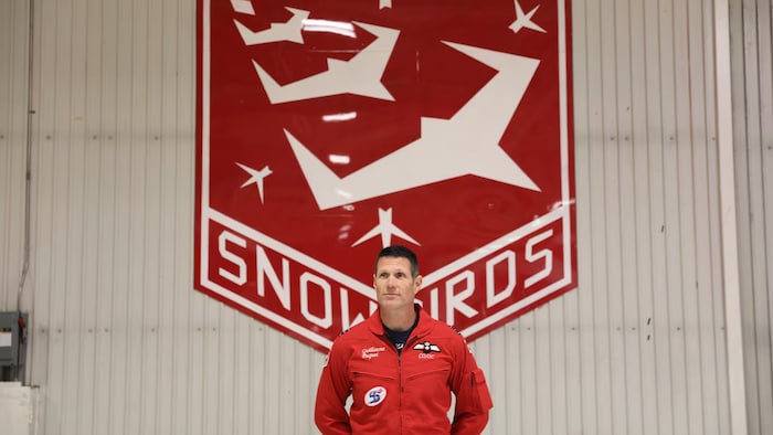 Un lieutenant-colonel, commandant de l'Équipe des Snowbirds, habillé d'une veste rouge se tient debout.
