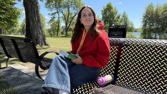 Zoé Asselin, assise sur un banc de parc, regarde l'objectif en souriant.
