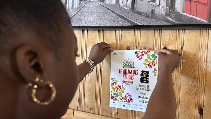 Une femme épingle à un mur une affiche annonçant les activités du Village des Nations. 