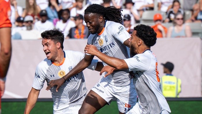Trois joueurs de soccer célèbrent un but.