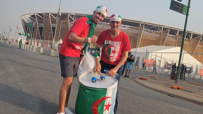 رجلان أمام مدخل ملعب وأحدهما يحمل طبلة.