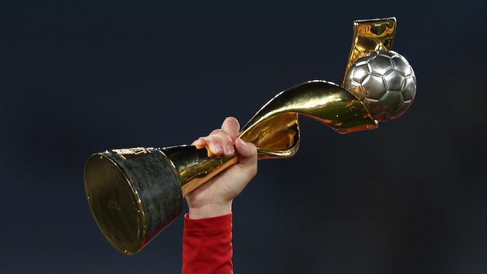 Close-up of a hand holding a trophy at arm's length.