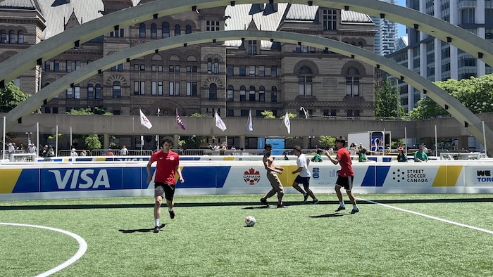 Des jeunes jouent au soccer sur un terrain de foot, place Nathan Phillips, à Toronto.