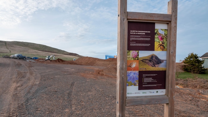 Une pancarte de la Société de conservation des Îles-de-la-Madeleine avec les terrains excavés en arrière.
