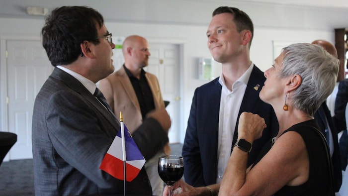 Éric Dow parle et sourit à deux autres personnes.