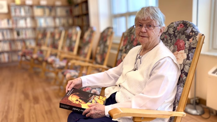 Une femme qui se berce avec un livre sur le pape dans les mains.