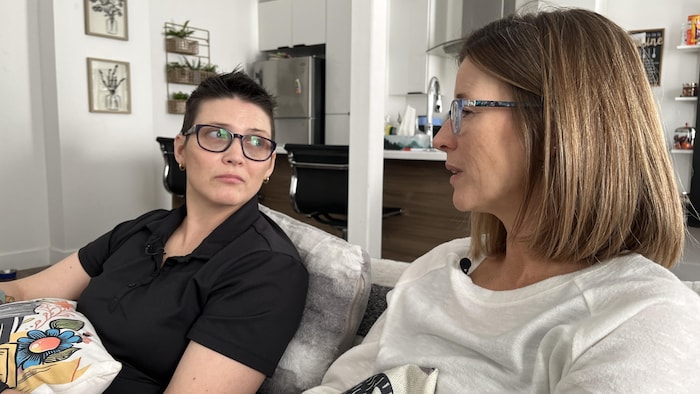 Karine regarde sa soeur Katia. Les deux sont assises sur un sofa. 