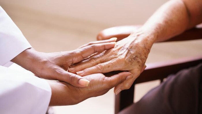 Une préposée tient la main d'une personne âgée