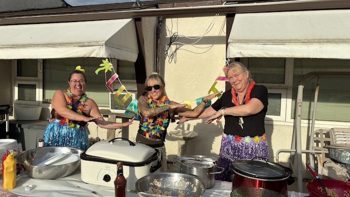 Trois femmes vêtues de jupes et de colliers hawaïens effectuent le hula en souriant.