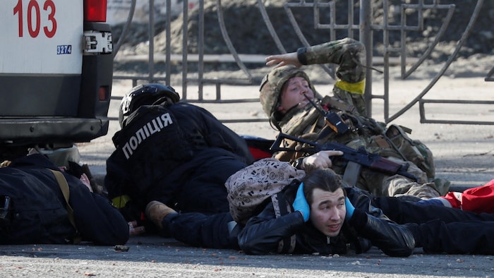 Un soldat ukrainien et un civil se couchent au sol et se couvrent les oreilles.