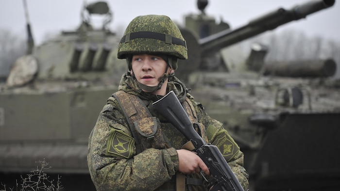 جندي يحمل بندقية وخلفه دبابة.