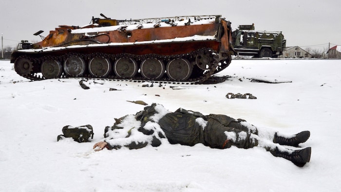 Un cadáver yace en la nieve cerca de un vehículo blindado.