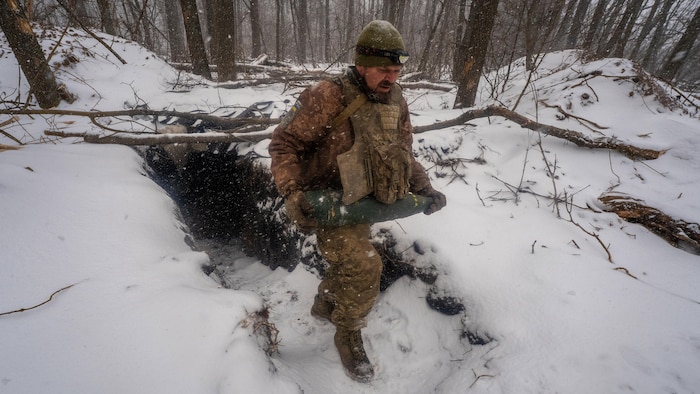 Un soldat ukrainien sort d'un bunker souterrain dans une forêt enneigée, obus à la main.