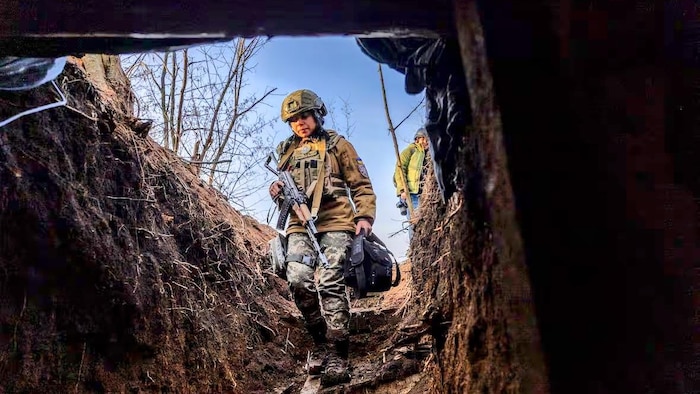 Une soldate ukrainienne armée rentre dans une tranchée.