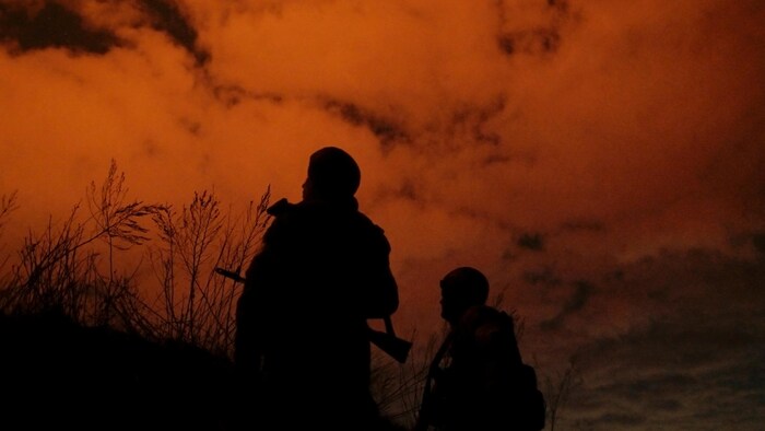Des soldats regardent au loin un incendie, la nuit.