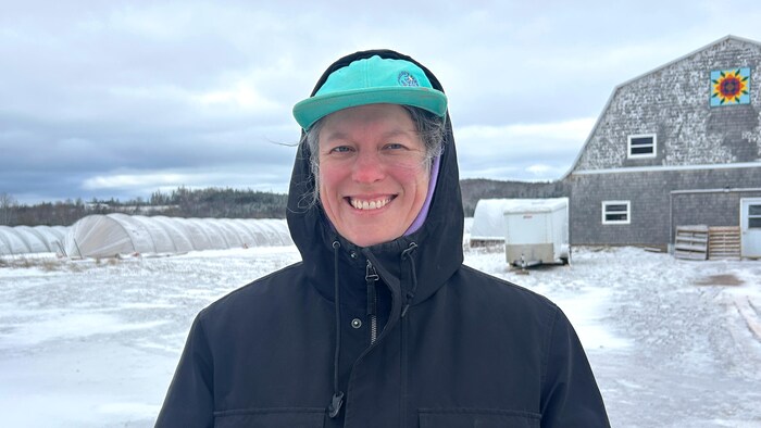 Debout dehors, dans la neige, avec une grange derrière, Soleil Hutchinson a le capuchon de son manteau d'hiver rabattu sur sa tête et elle sourit.