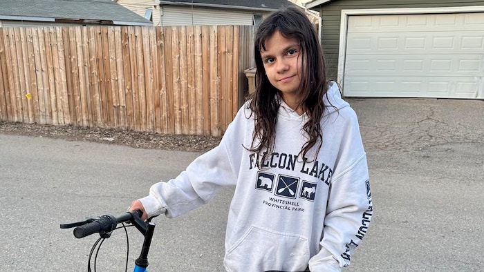 Une jeune enfant tient un vélo.
