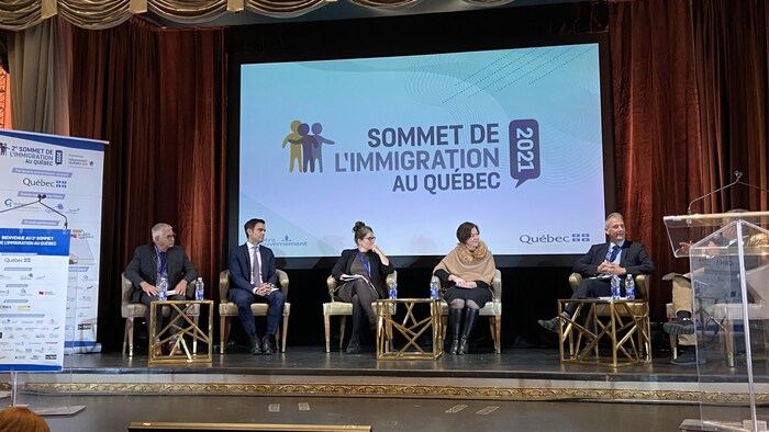 Cinq personnes assises sur des chaises en haut d'une estrade.