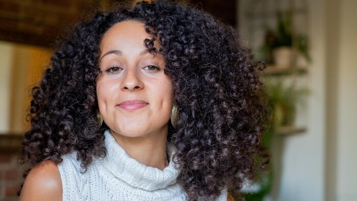 Une femme avec des cheveux bruns, bouclés, sourit.