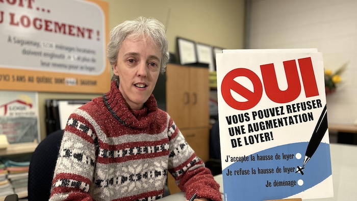 Une femme devant une affiche disant qu'on peut refuser une augmentation de loyer.