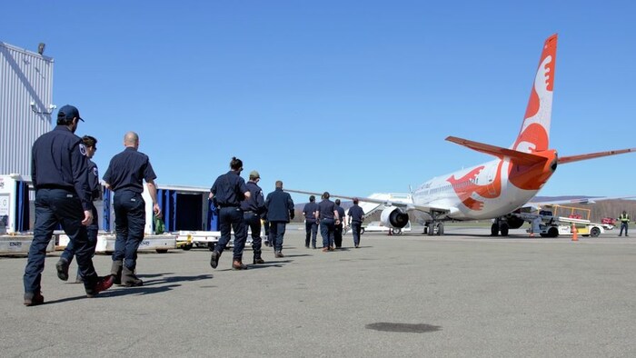 Des pompiers en uniforme se dirigent vers un avion avant l'embarquement. 