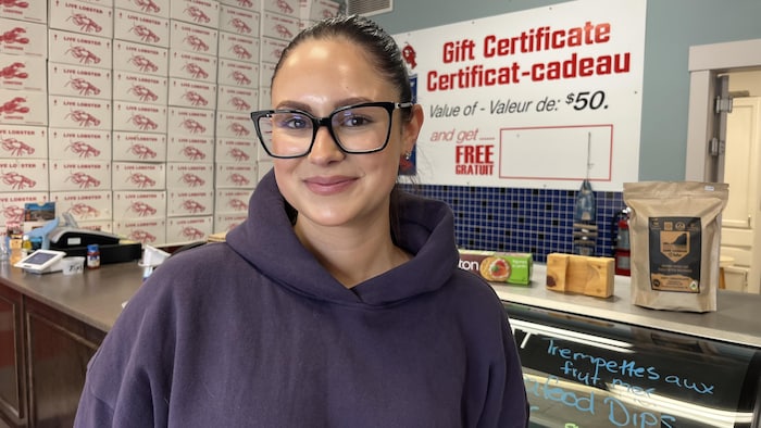 Une femme sourit à la caméra, devant un comptoir dans une poissonnerie.