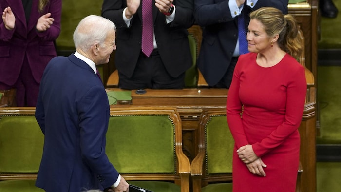 Sophie Grégoire Trudeau et Joe Biden se sourient devant des bancs du Parlement tandis que des personnes applaudissent à l'arrière.