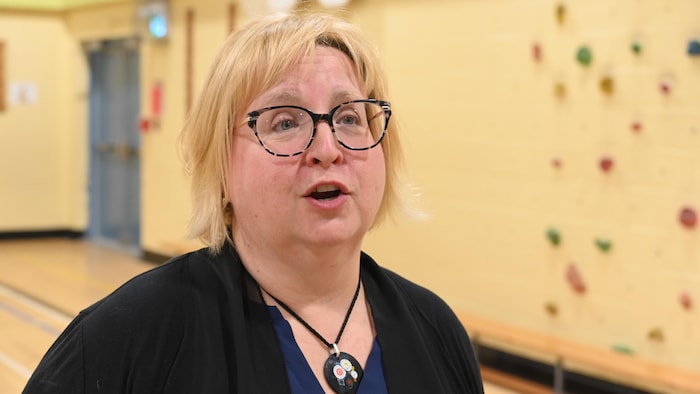 Une personne aux cheveux blonds en entrevue. Elle porte des lunettes. 