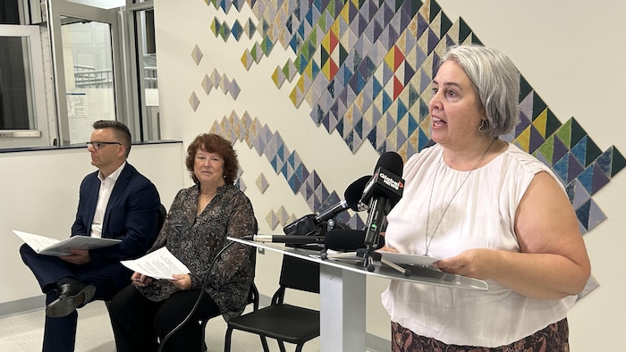 La directrice parle dans le micro, deux personnes assises à sa gauche.