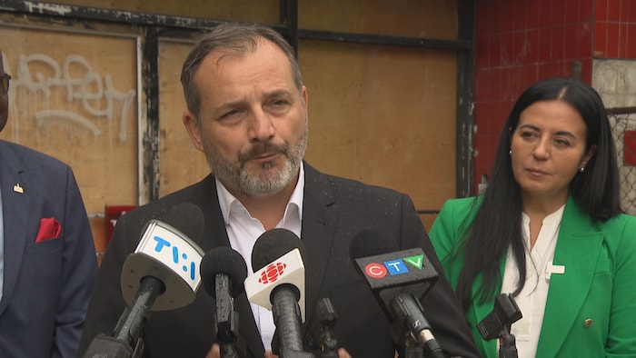 Un homme parle au micro devant une femme derrière lui.