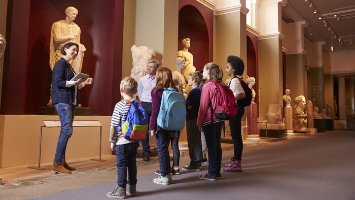 Des enfants écoutent une guide dans un musée, devant une statue.