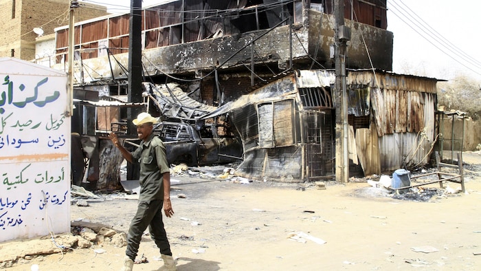 Un soldat fait un salut de la main aux abords d'un immeuble calciné et quasi détruit.