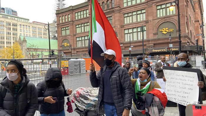 Un homme portant un drapeau soudanais et plusieurs personnes autour de lui.