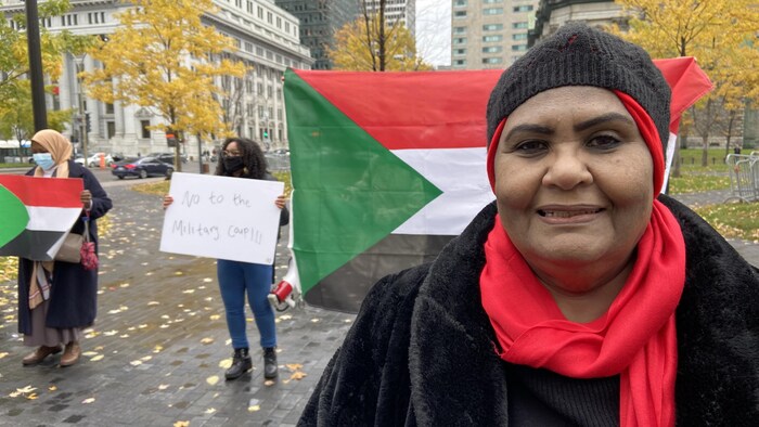 Une femme debout dans un parc et un drapeau soudanais derrière elle