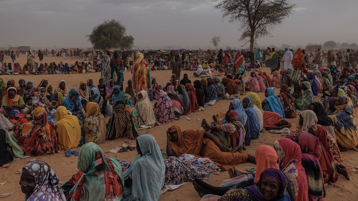 Des centaines de femmes vêtues de pagnes colorés sont assises par terre dans une portion désertique.