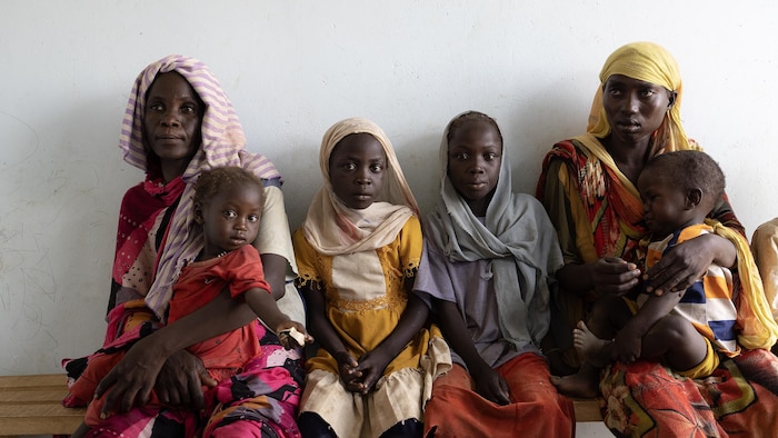 Des femmes et des enfants réfugiés soudanais attendent, assis sur un banc.