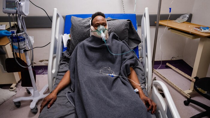 Une personne portant un masque allongée dans un lit d'hôpital.