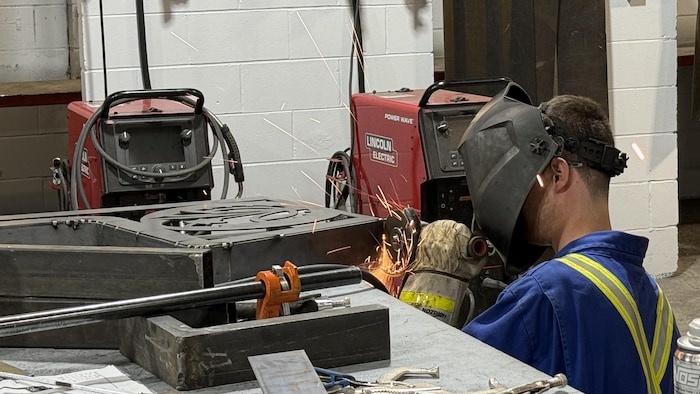 Avec son casque, un élève travaille avec une meuleuse sur une pièce qu'il assemble.
