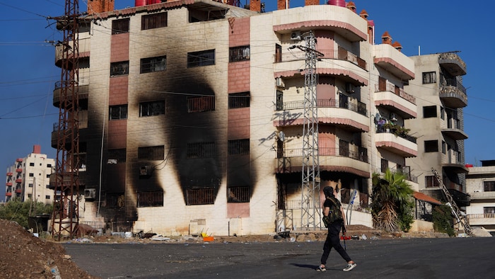  Un homme armé passe près d'un bâtiment incendié.