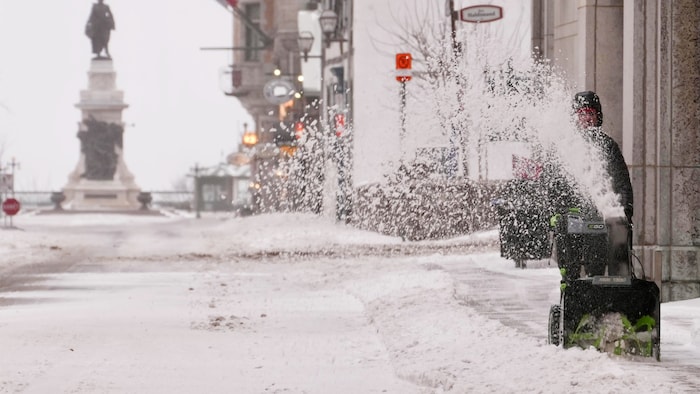 Un individu déneige un trottoir.